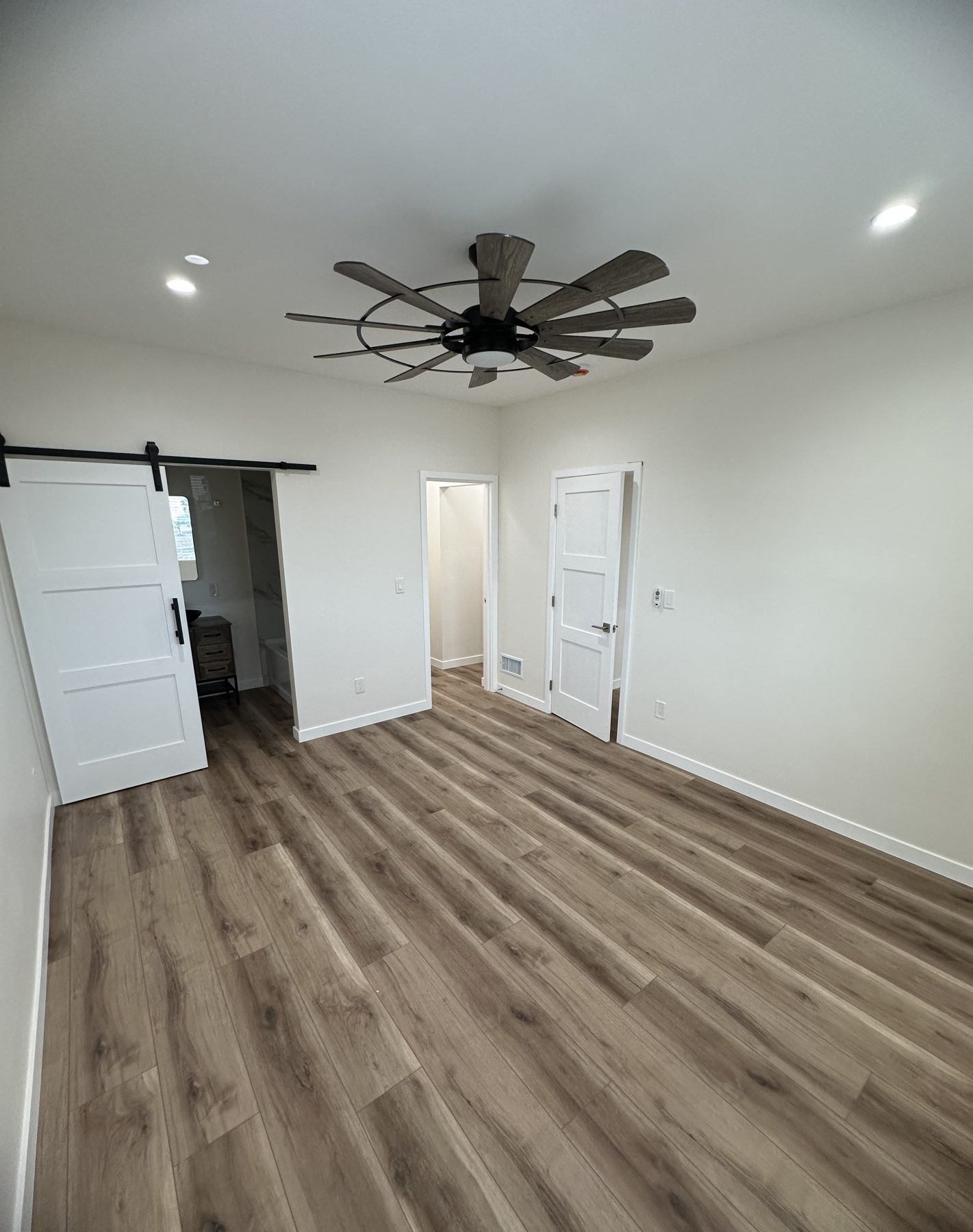 Primary bedroom with ceiling fan and barn door to the bathroom at 1148 S Rimpau Blvd