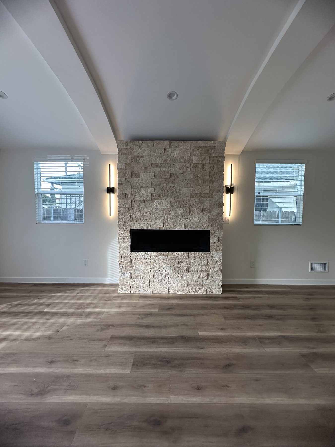 Remote-controlled fireplace set in a stacked-stone wall with lit sconces at 1148 S Rimpau Blvd