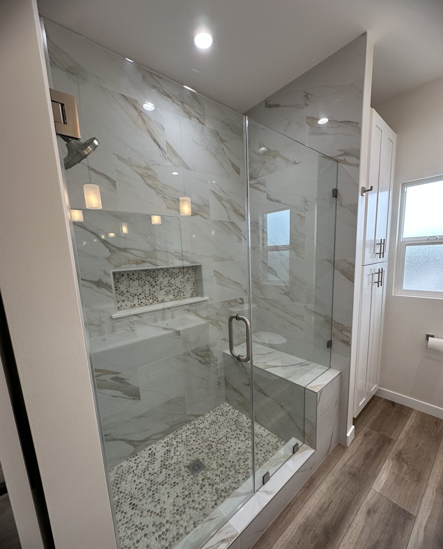 Walk-in glass shower with marble-look tile, bench and pebble floor at 1148 S Rimpau Blvd